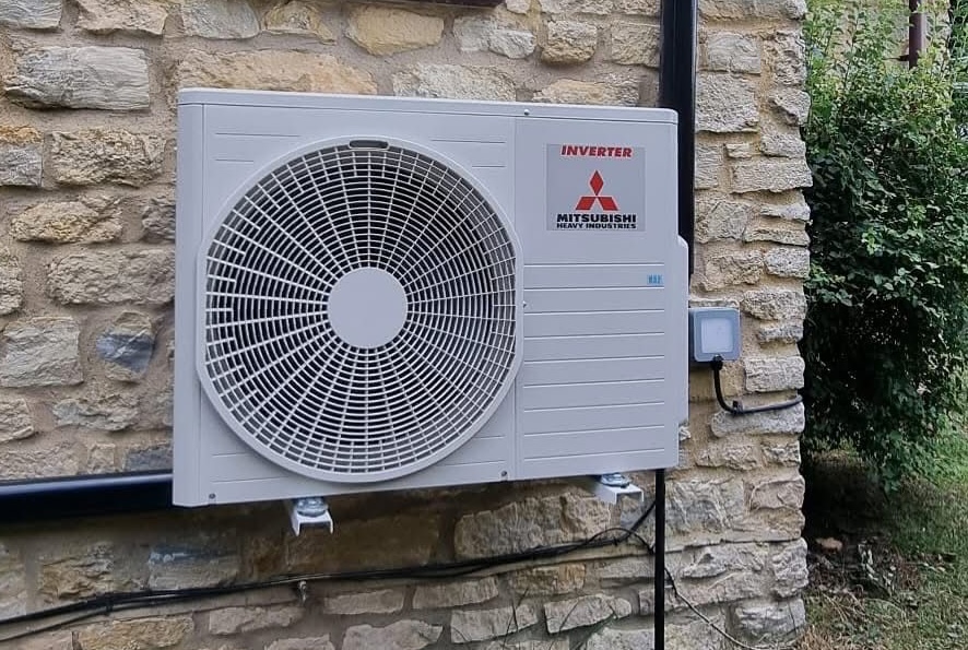 Outdoor air conditioning unit attached to the side of a stone cottage